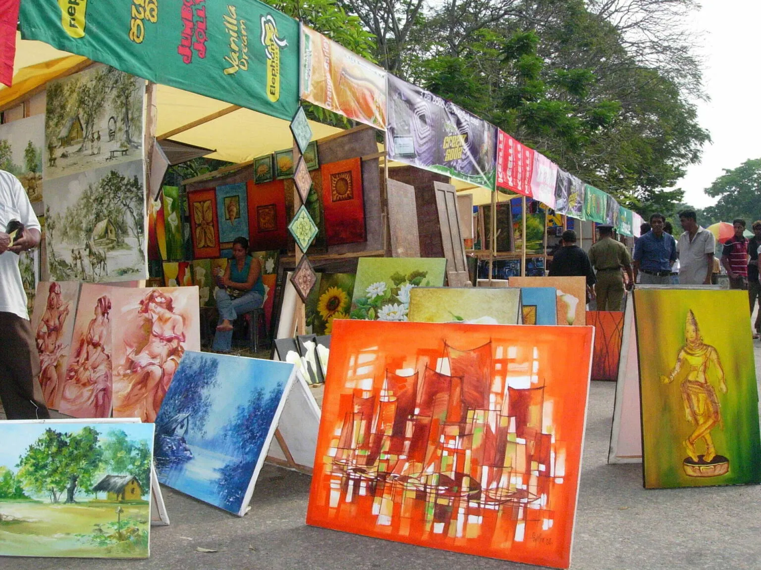 A man stands before a tent adorned with various paintings, showcasing artistic creativity in an outdoor setting.