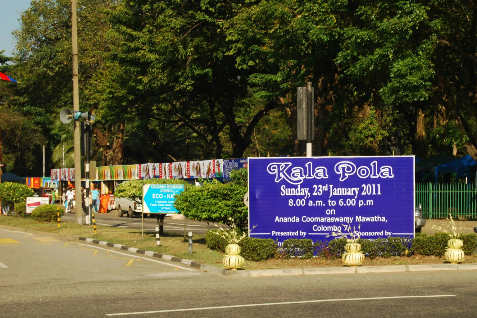 A street sign surrounded by kalapola posters, contributing to the lively streetscape.