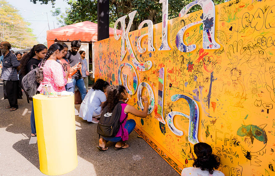 A group of people stands by a graffiti-covered wall, actively drawing and adding their own images to the artwork.